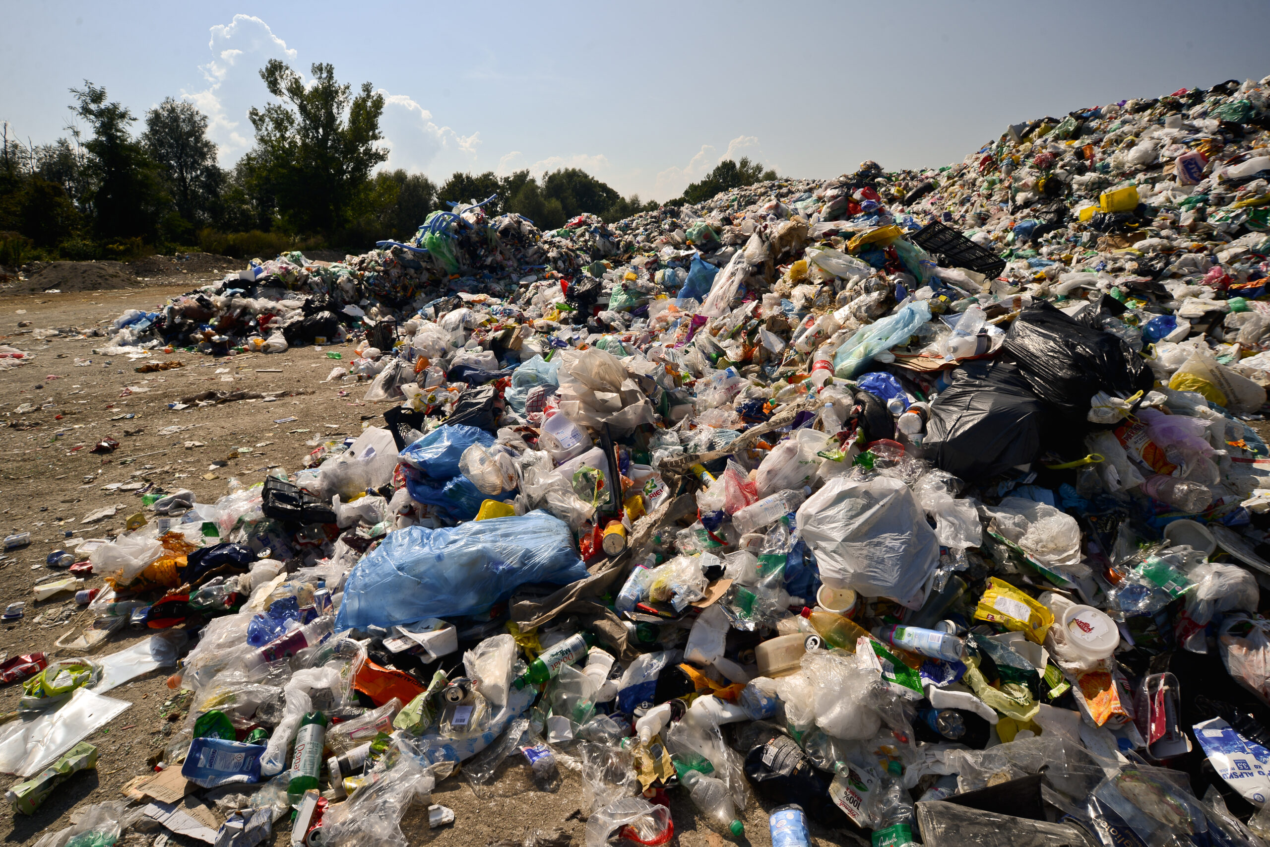 Montañas de residuos plásticos acumulados en un vertedero al aire libre, con bolsas, envases y botellas esparcidos sobre el suelo bajo la luz del sol.
