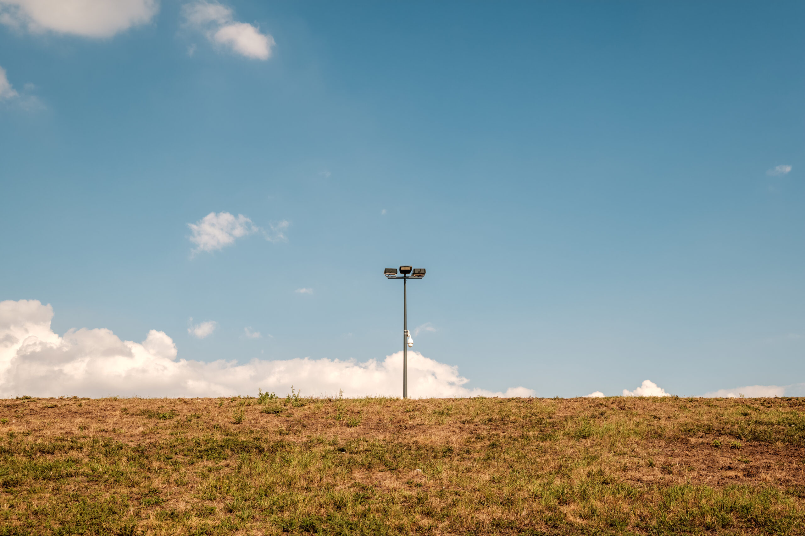 Farola solitaria erguida en medio de un campo seco con cielo azul despejado y nubes dispersas al fondo.