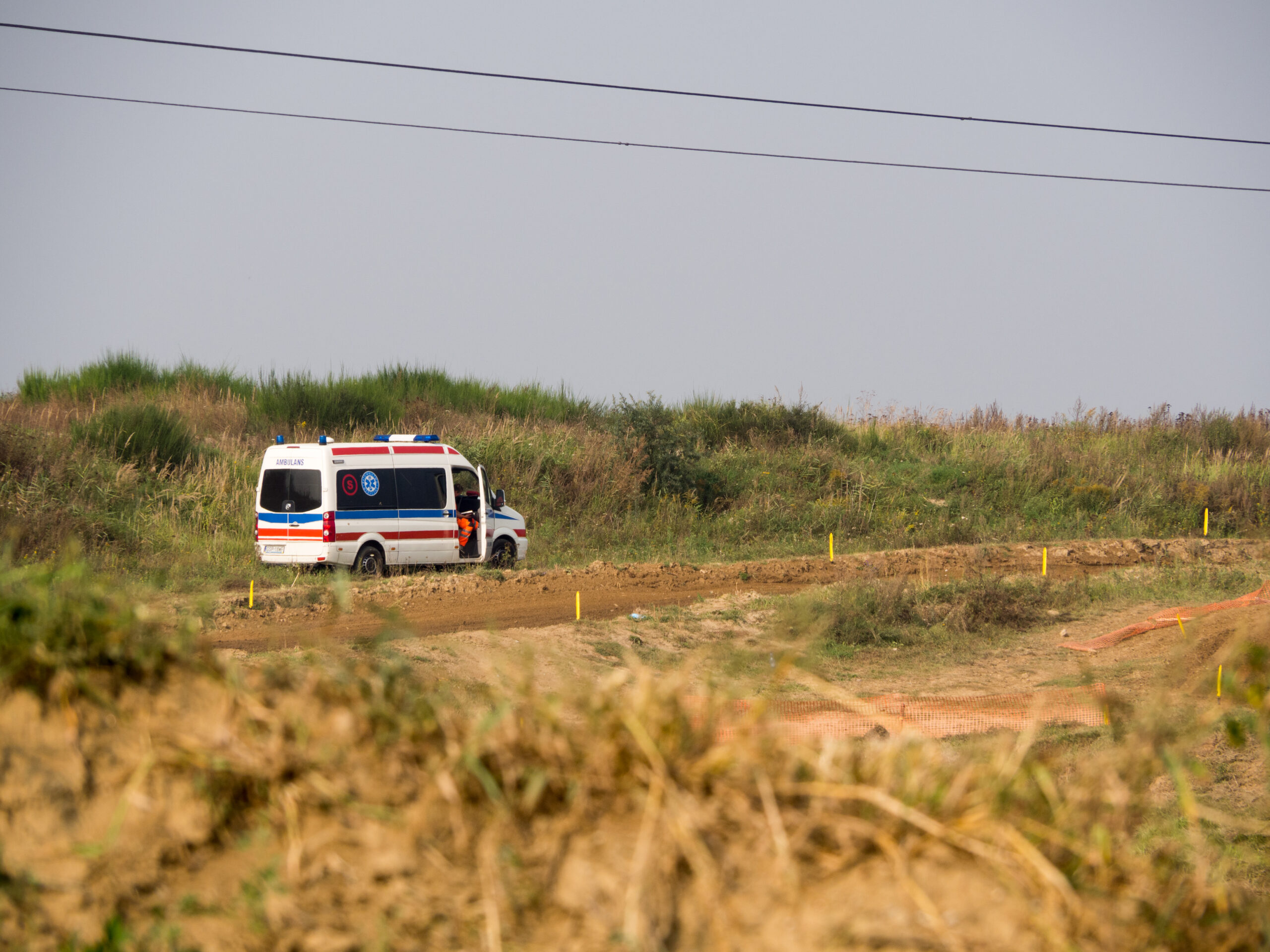 Ambulancia estacionada en un camino de tierra rodeado de pastizales, con un trabajador de emergencia visible junto a la puerta abierta.